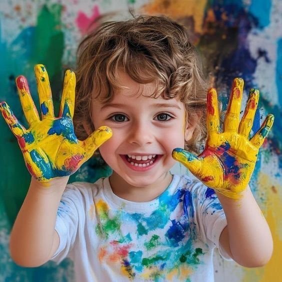 Smiling child with hands painted in bright yellow, blue, and red paint